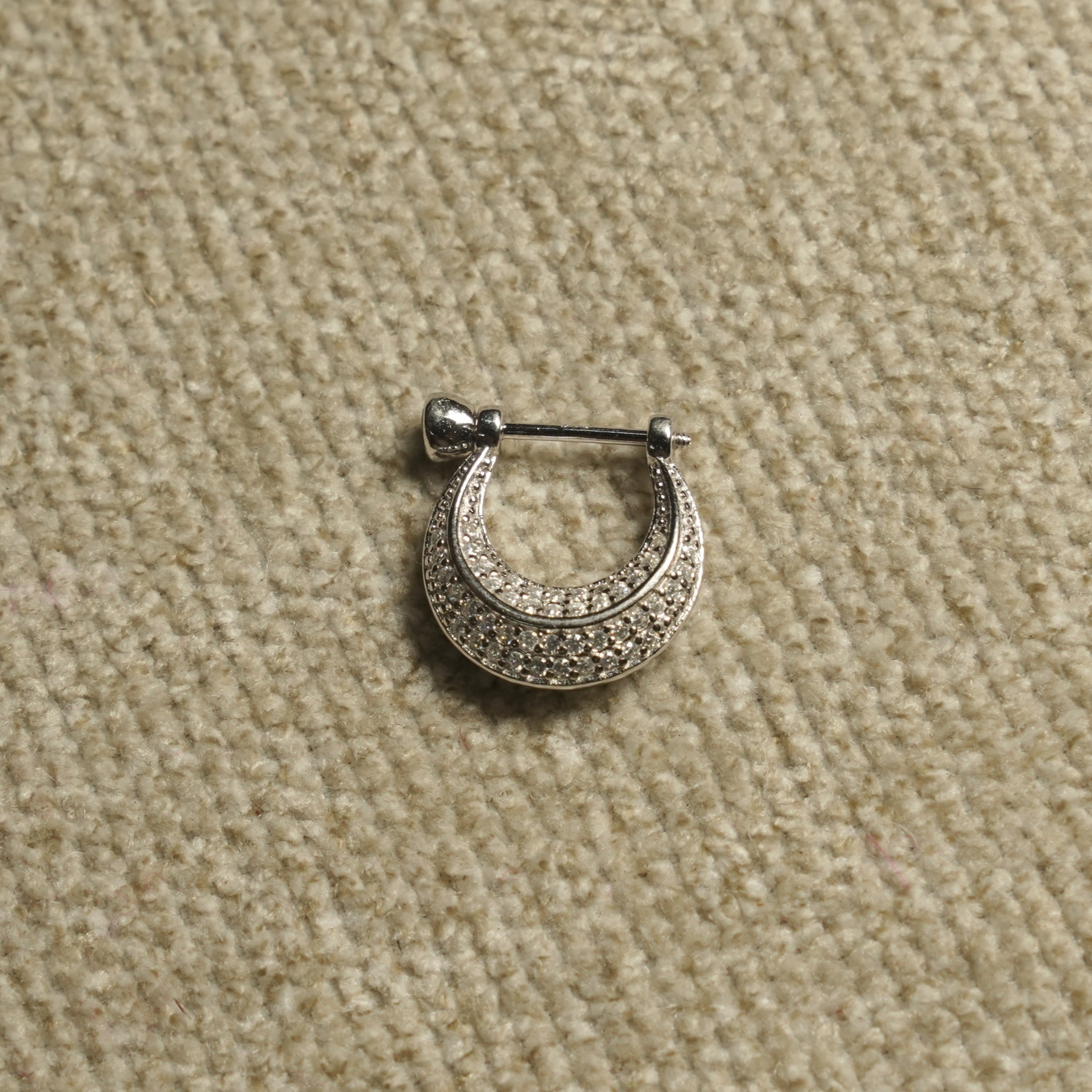 Single sterling silver Bejewelled crescent hoop earring shown up close, its rows of cubic zirconia following the curve, on beige woven fabric.