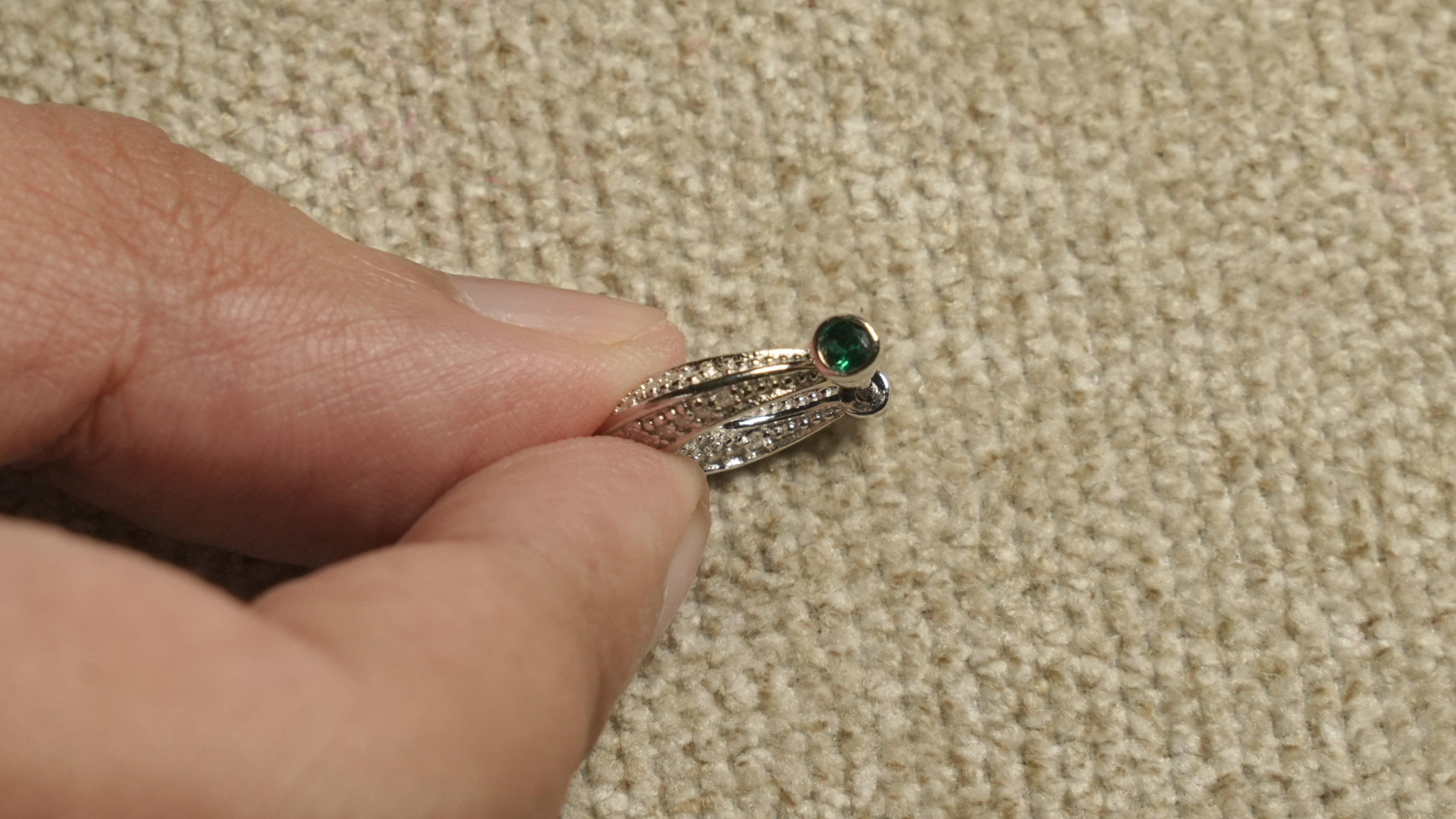 Sterling silver Bejewelled earring held between fingertips, showing the beaded texture and a small green cubic zirconia accent.