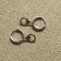 Pair of sterling silver hinged hoop earrings, each with a small bead-textured open-circle charm holding a tiny leaf detail, on beige woven fabric.