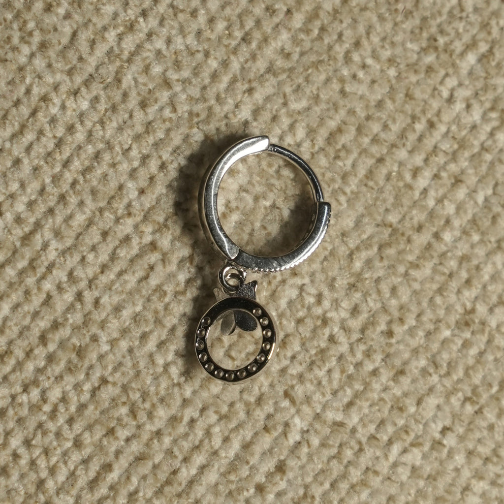 Close view of a single sterling silver hoop earring with its beaded open-circle drop and leaf detail, on beige woven fabric.