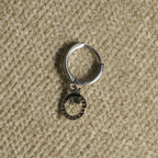 Close view of a single sterling silver hoop earring with its beaded open-circle drop and leaf detail, on beige woven fabric.