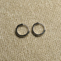 Pair of slim sterling silver huggie hoop earrings with hinged closures, laid side by side on beige woven fabric.