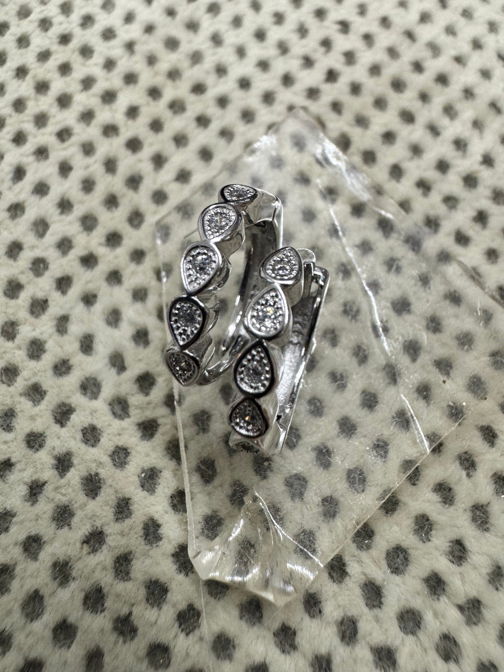 Pair of sterling silver huggie hoop earrings with bezel-set cubic zirconia in teardrop collets, resting on a clear glass block.