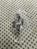 Pair of sterling silver huggie hoop earrings with bezel-set cubic zirconia in teardrop collets, resting on a clear glass block.