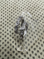 Pair of sterling silver huggie hoop earrings with bezel-set cubic zirconia in teardrop collets, resting on a clear glass block.