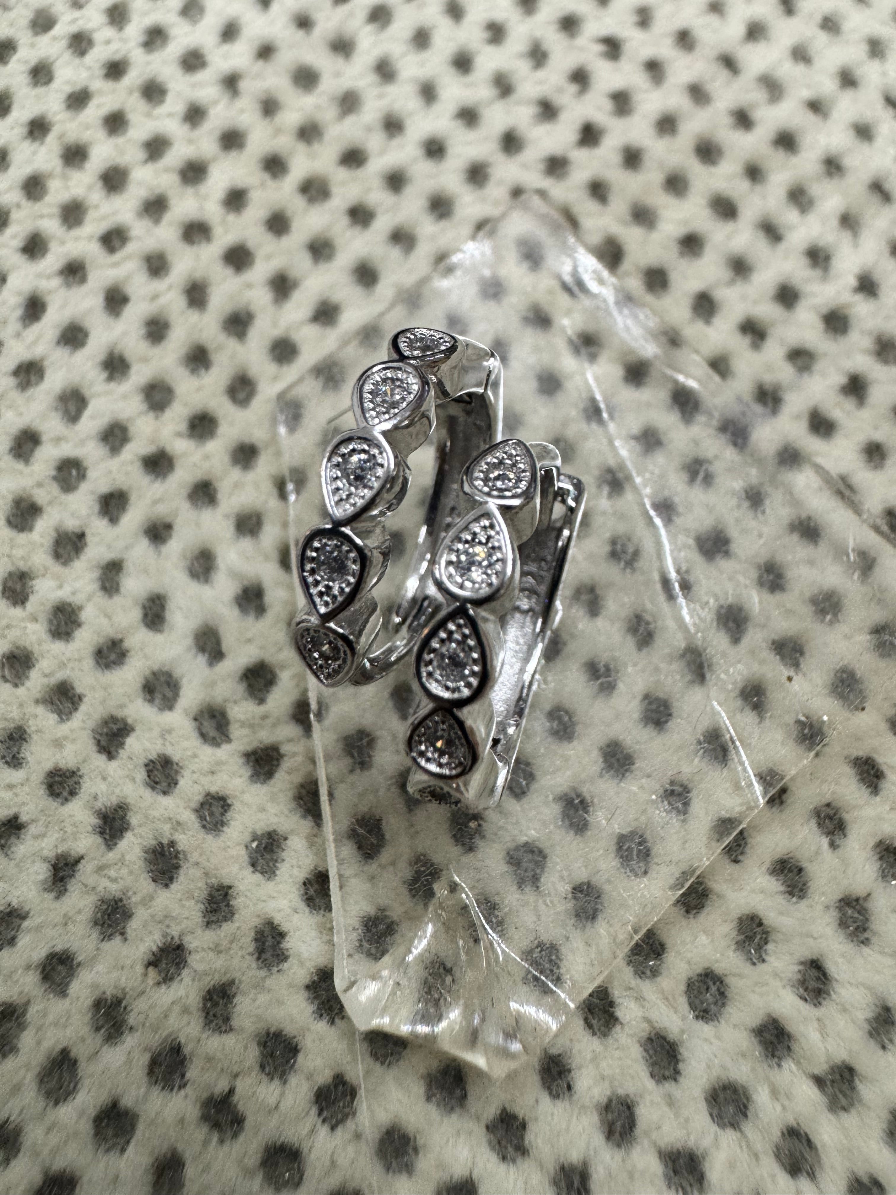 Pair of sterling silver huggie hoop earrings with bezel-set cubic zirconia in teardrop collets, resting on a clear glass block.