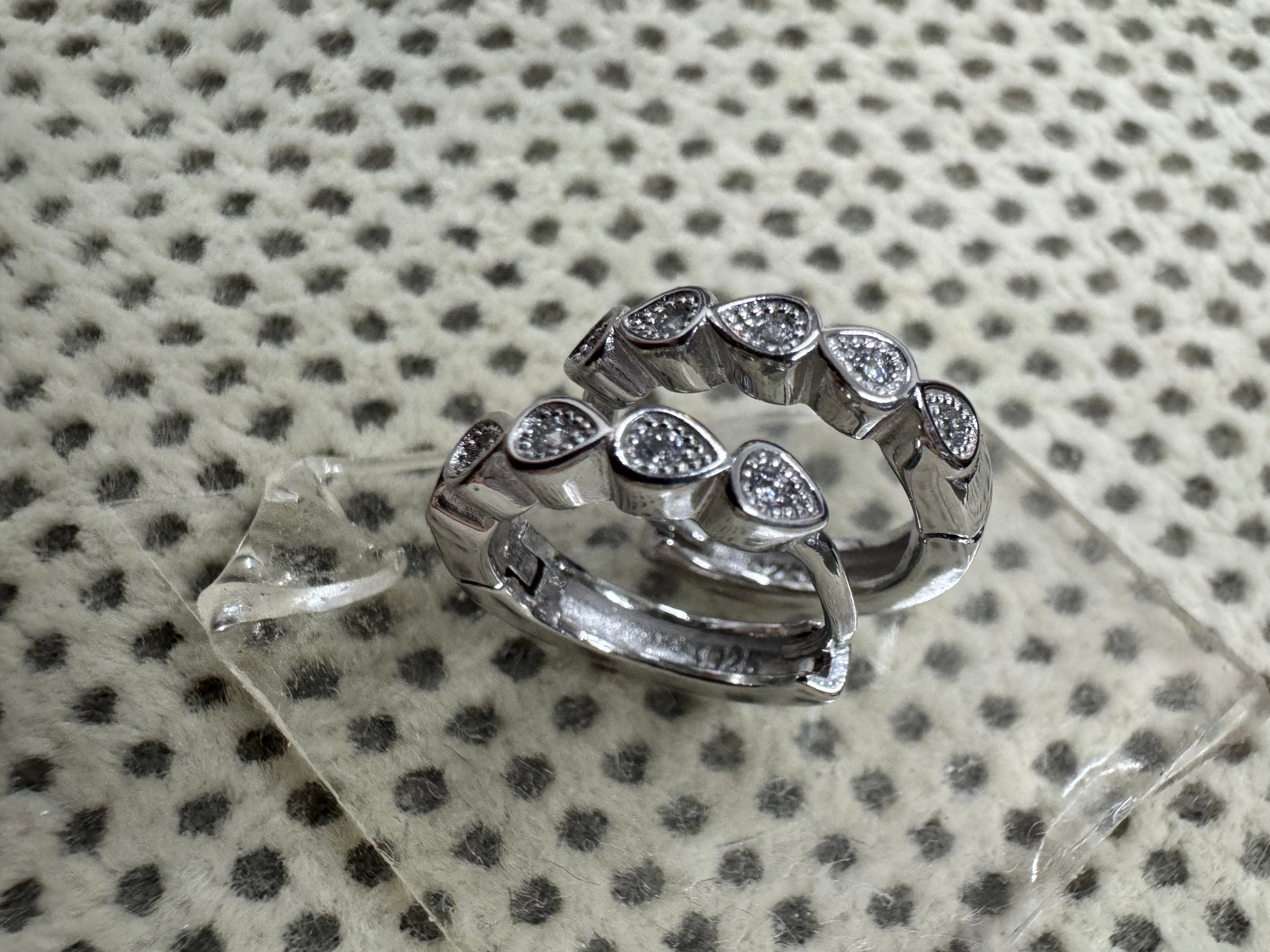 The sterling silver cubic zirconia huggie hoops on clear glass, with the 925 stamp visible inside the plain rear section.