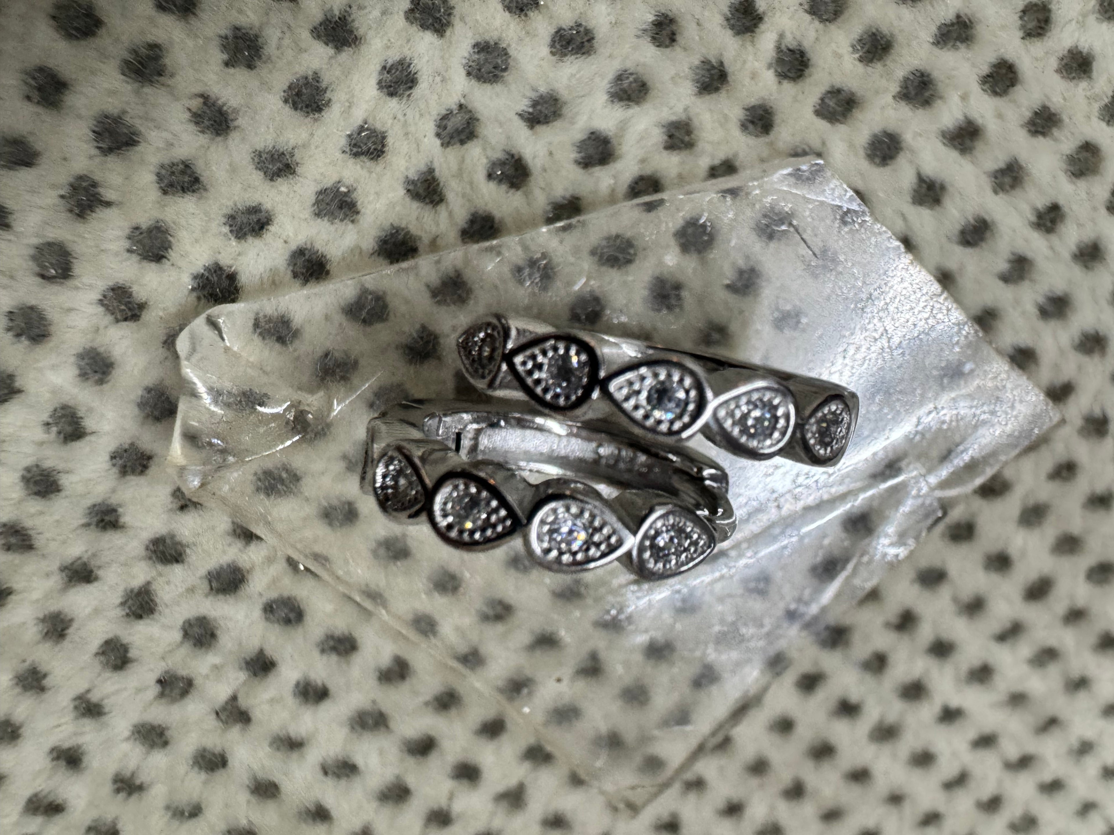 Both sterling silver huggie hoop earrings seen from above on a glass block over spotted grey fabric.