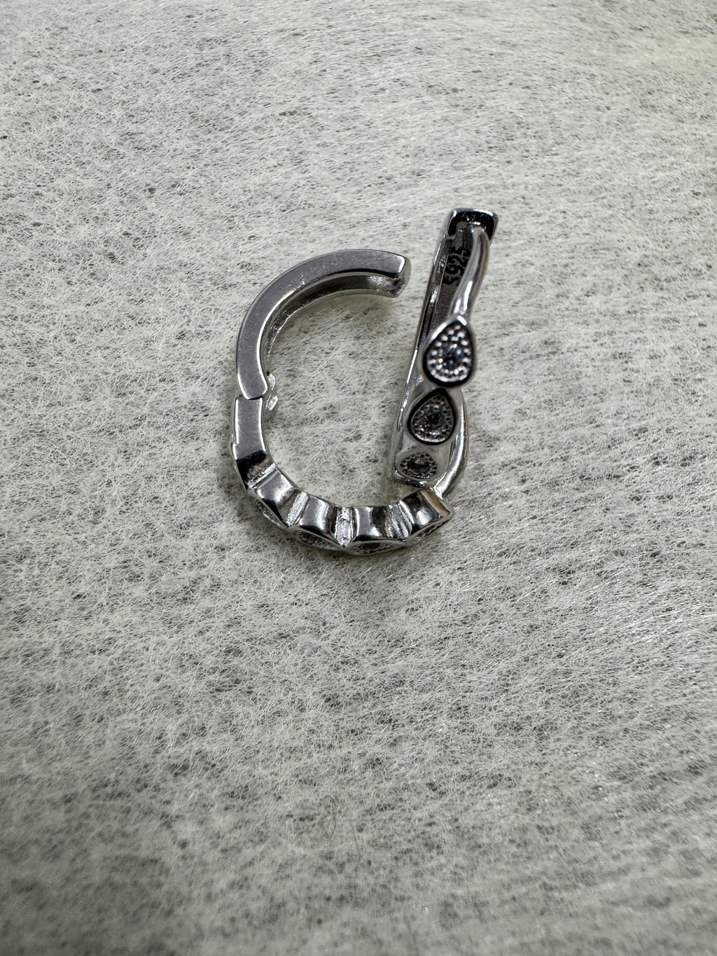 Single sterling silver huggie hoop earring opened at the hinge, showing the latch back and the teardrop bezels.