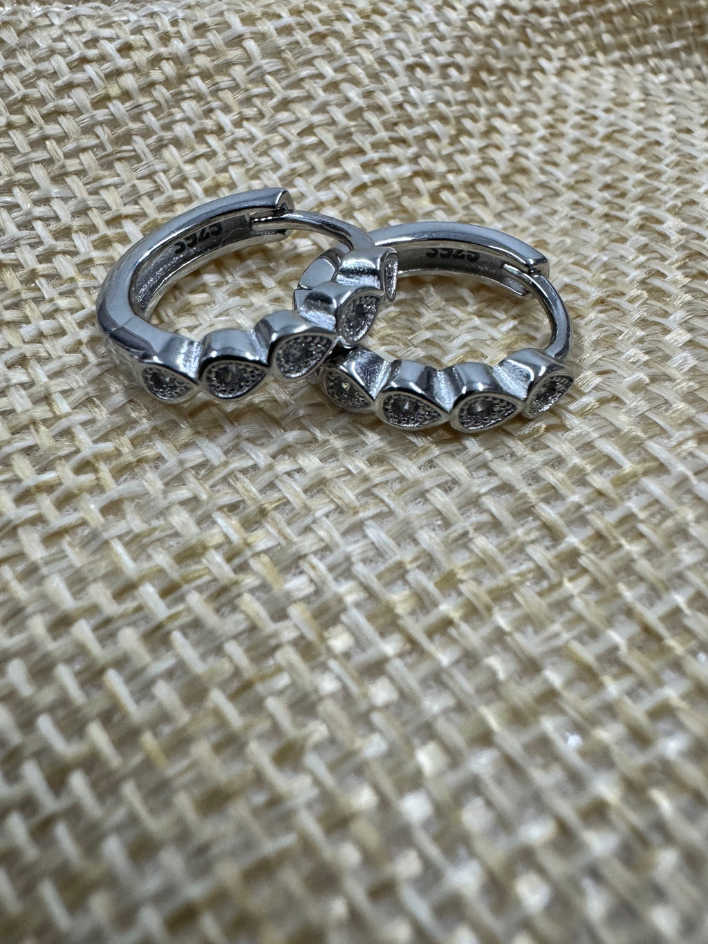 Close view of the sterling silver huggie hoops on woven jute, the row of bezel-set cubic zirconia along the front.