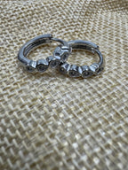 Close view of the sterling silver huggie hoops on woven jute, the row of bezel-set cubic zirconia along the front.
