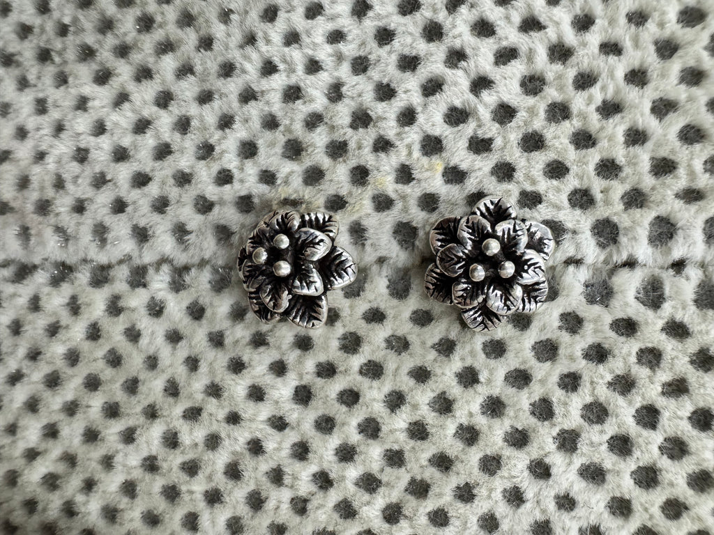 Pair of oxidised sterling silver flower stud earrings on spotted grey fabric.
