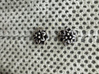 Pair of oxidised sterling silver flower stud earrings on spotted grey fabric.