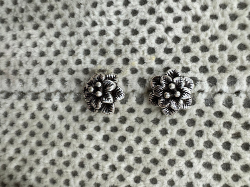 Pair of oxidised sterling silver flower stud earrings on spotted grey fabric.