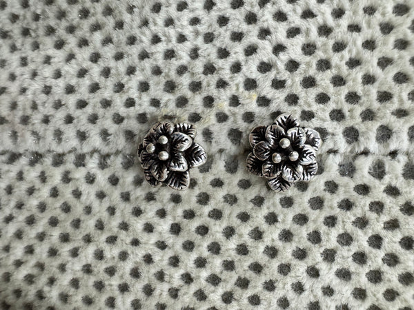 Pair of oxidised sterling silver flower stud earrings on spotted grey fabric.