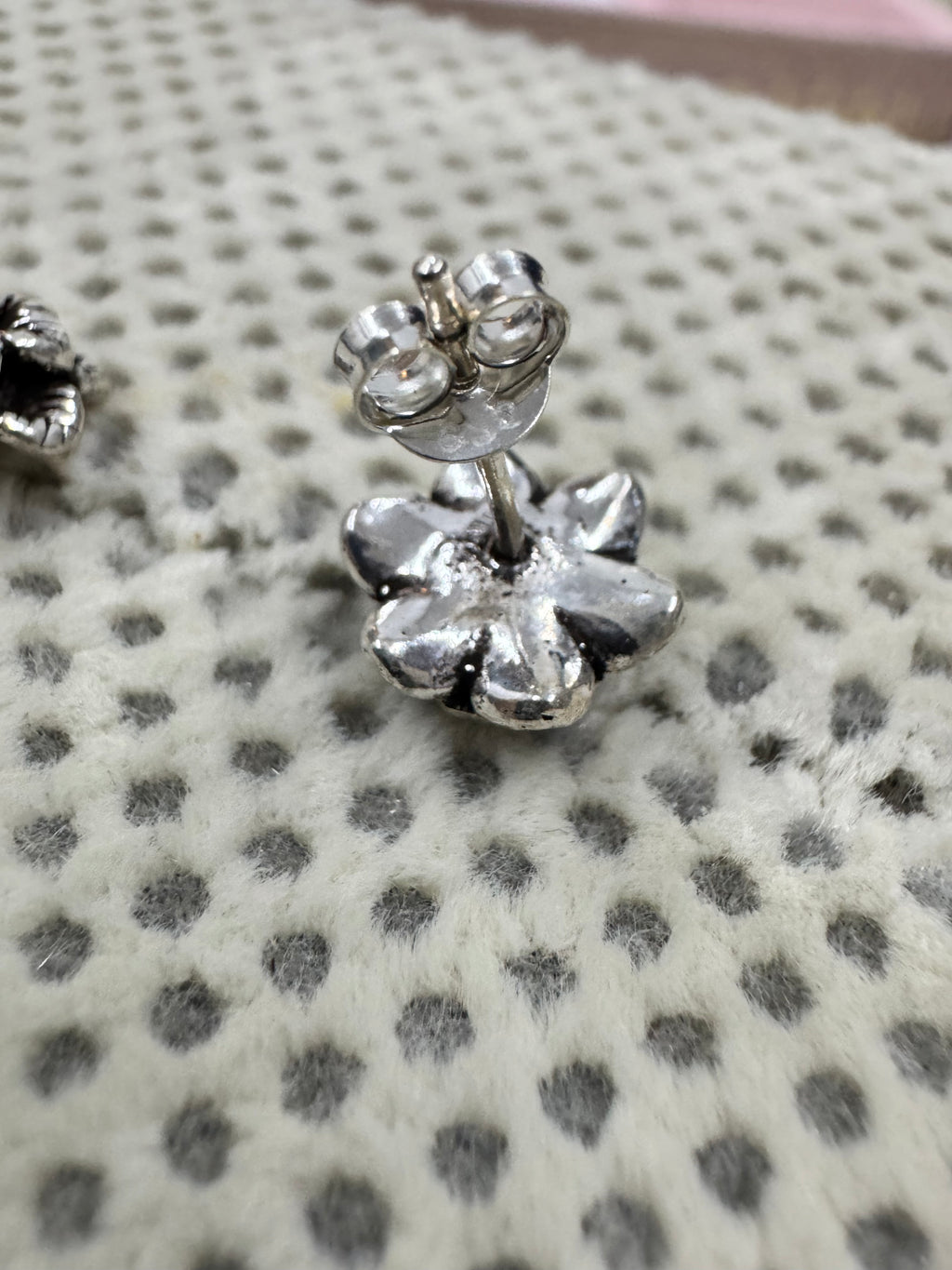 Side view of one oxidised sterling silver flower stud with its straight post and butterfly back.