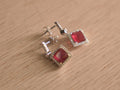 Pair of sterling silver drop earrings with square imitation ruby glass stones inside halos of small colourless stones.