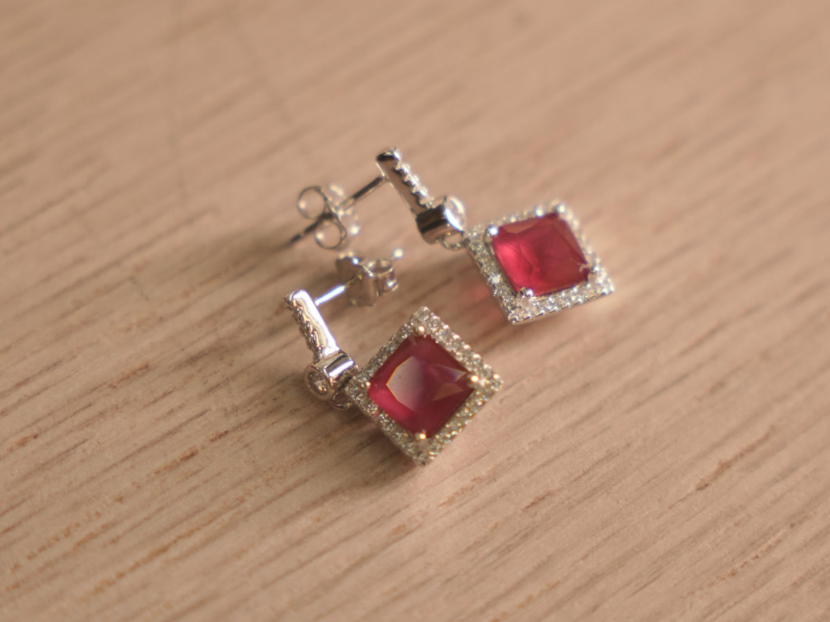 Pair of sterling silver drop earrings with square imitation ruby glass stones inside halos of small colourless stones.
