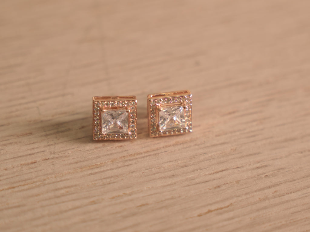 Angled view of the rose-tone square halo studs, showing the prong set centres and stepped halo edges.