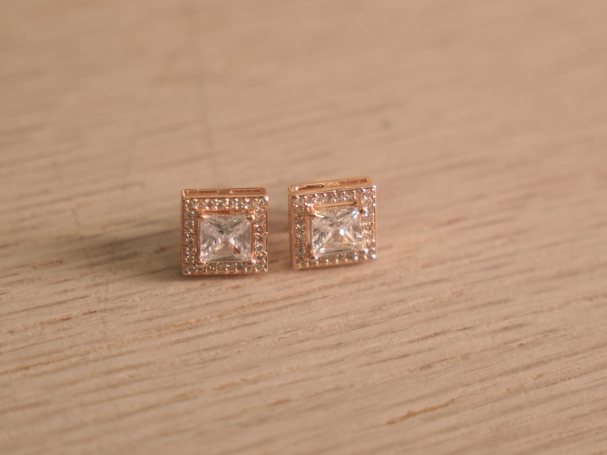 Angled view of the rose-tone square halo studs, showing the prong set centres and stepped halo edges.