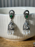 Single jhumka held upright, showing the leafy stud top and the green teardrop at the crown of the dome.
