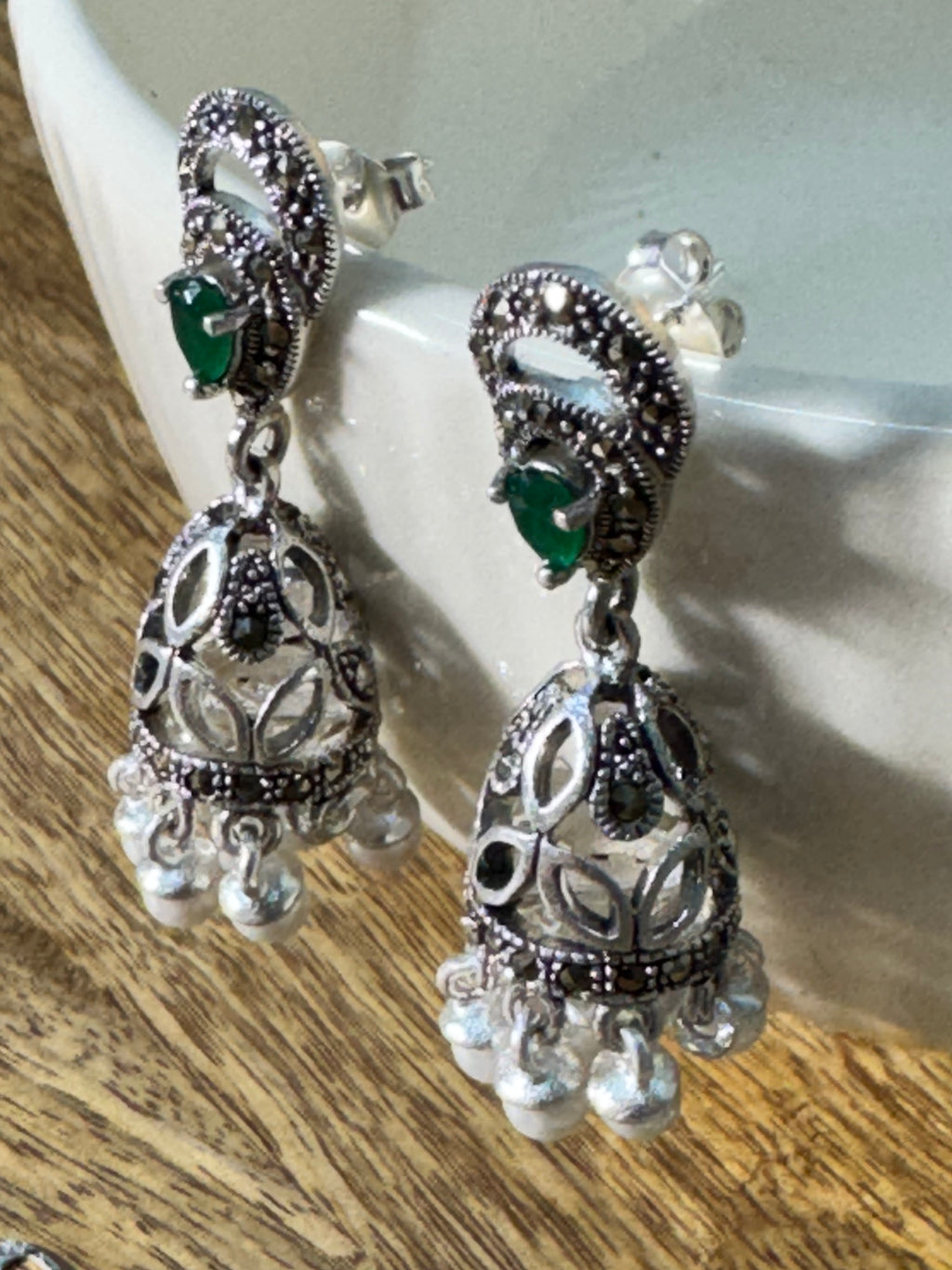 The green glass stone jhumkas resting together, fringes fanned on a plain background.