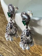 The green glass stone jhumkas resting together, fringes fanned on a plain background.