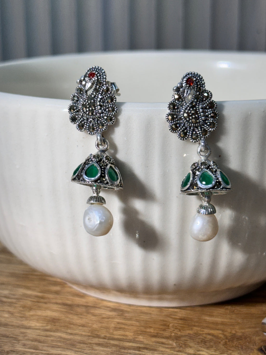 Pair of sterling silver peacock stud jhumkas with green glass stone cones and white drop beads.