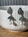 Pair of sterling silver peacock stud jhumkas with green glass stone cones and white drop beads.