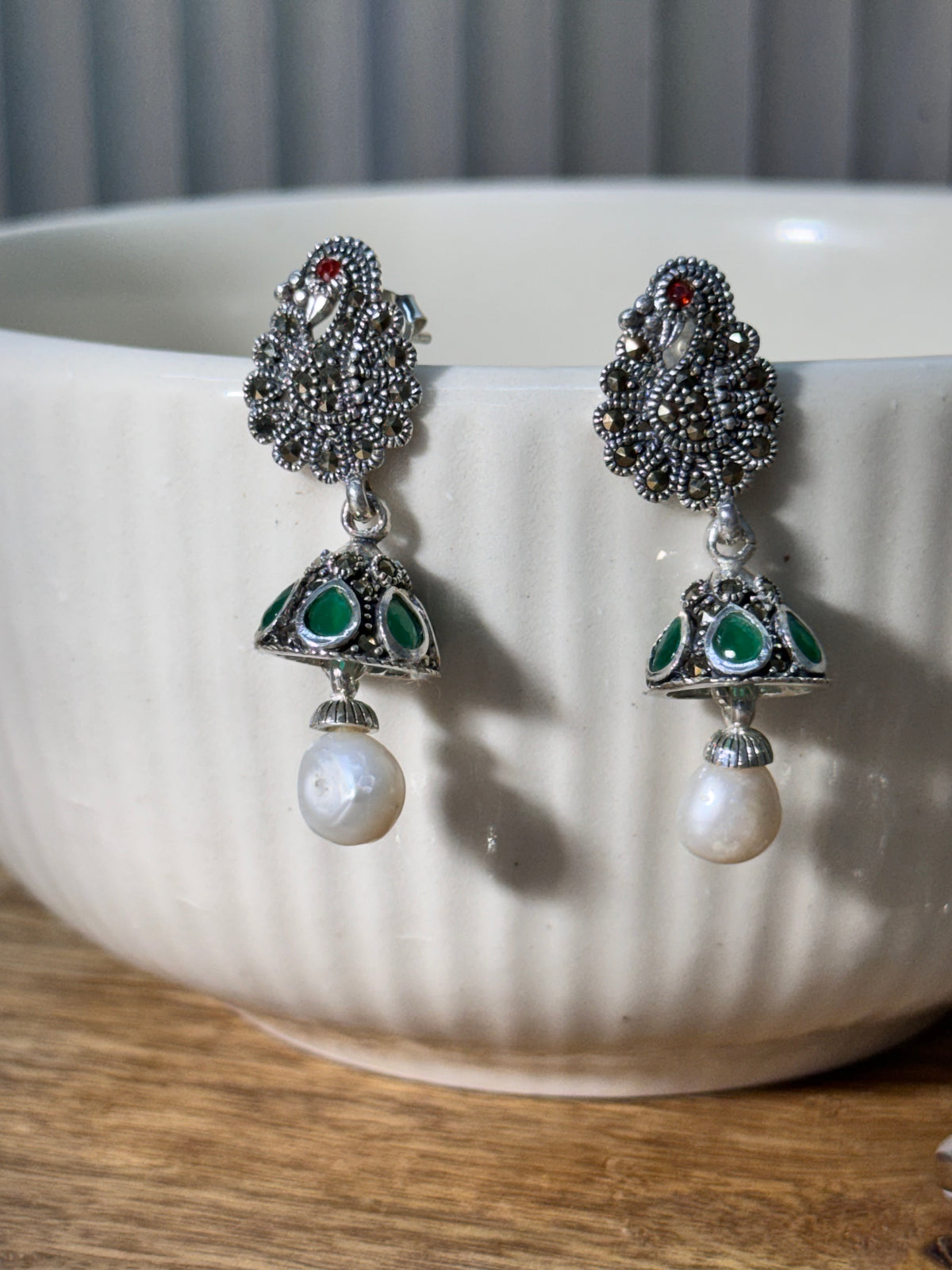 Pair of sterling silver peacock stud jhumkas with green glass stone cones and white drop beads.
