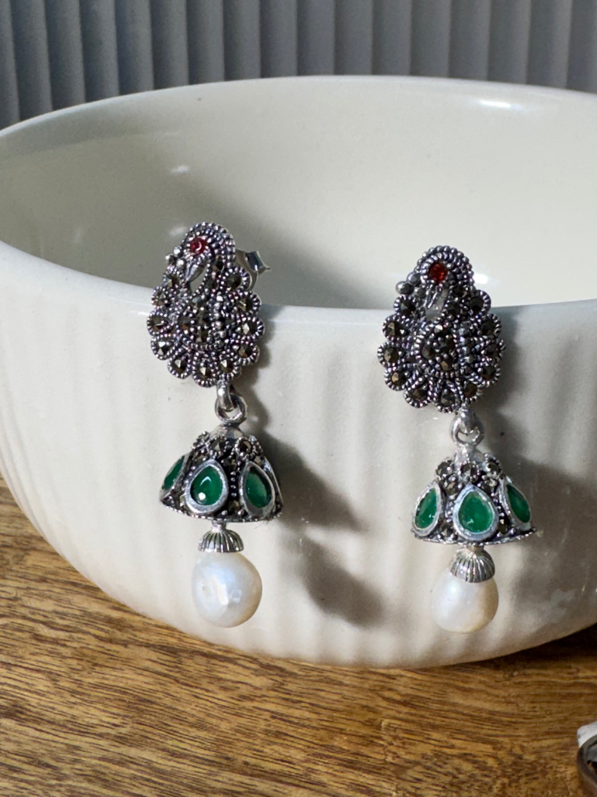 Close view of the peacock stud with its red accent eye, above the green glass stone cone.