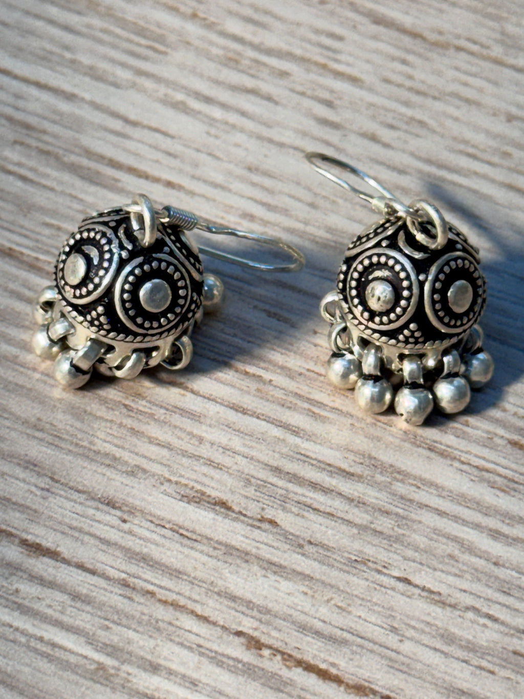 Oxidised jhumkis laid on woven fabric, showing the french hooks and dome panels.