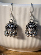 Both oxidised ghungroo jhumkis resting on a wooden surface, domes facing forward.