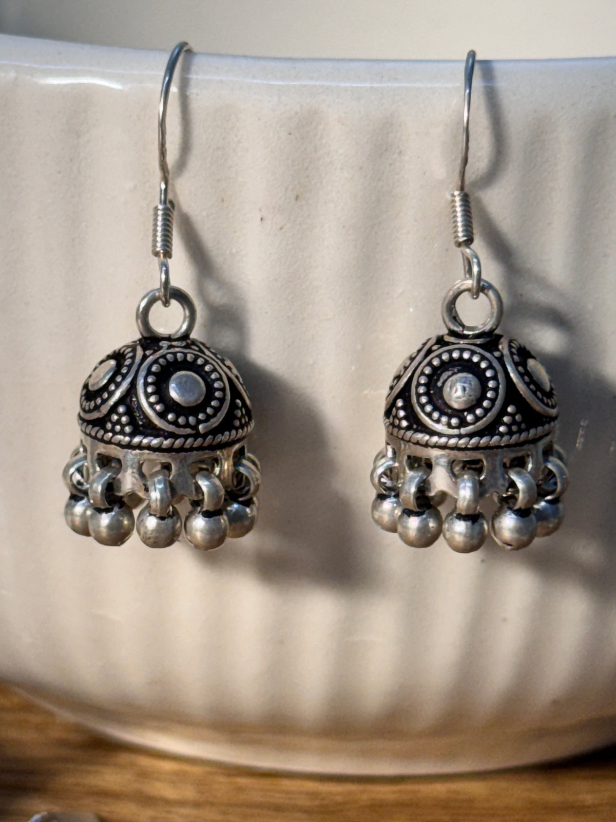 Both oxidised ghungroo jhumkis resting on a wooden surface, domes facing forward.