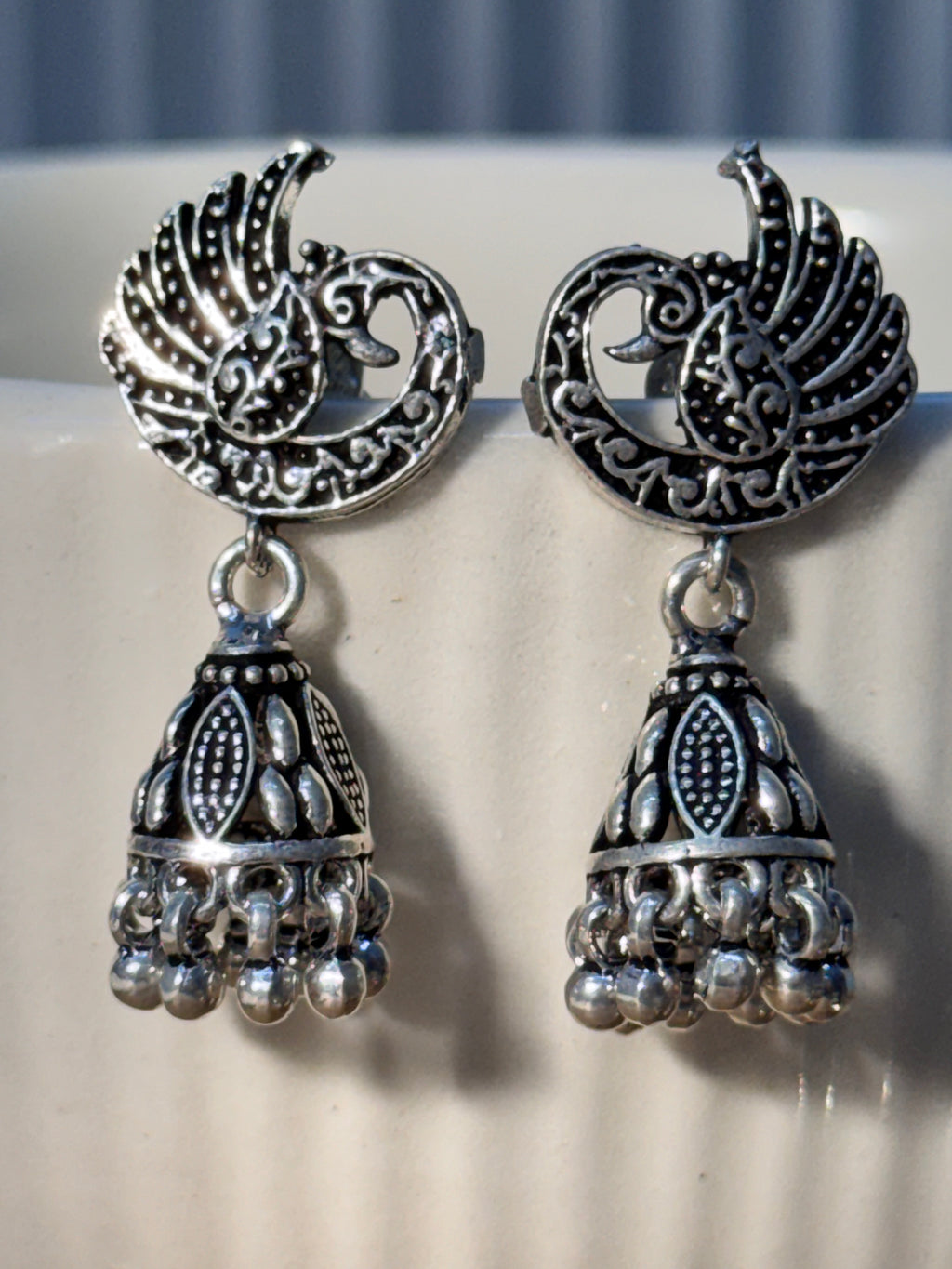 Pair of oxidised sterling silver crescent stud jhumkas with facing peacock detail.