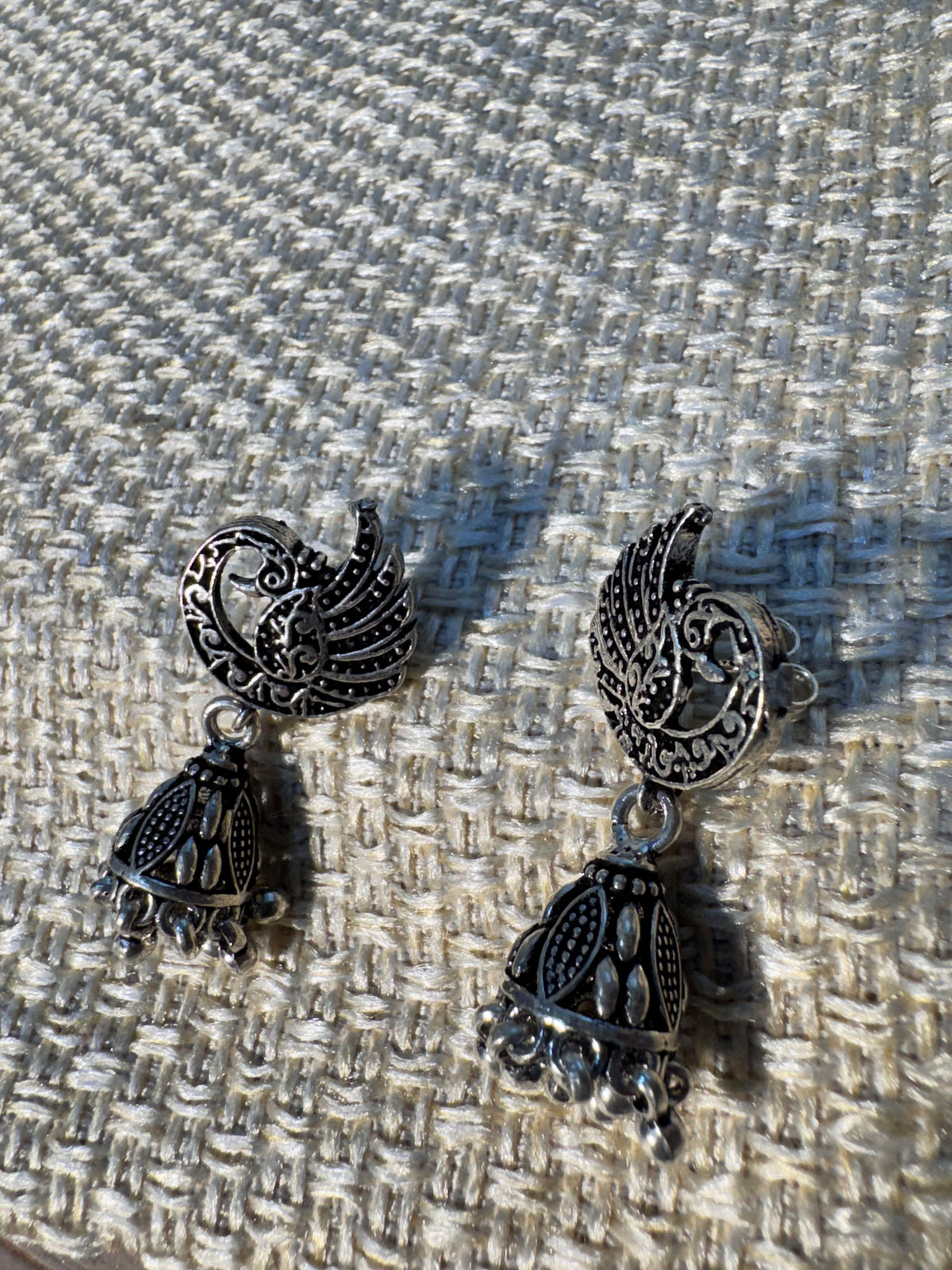 The peacock crescent jhumkas laid together, showing the beaded cones and fringes.