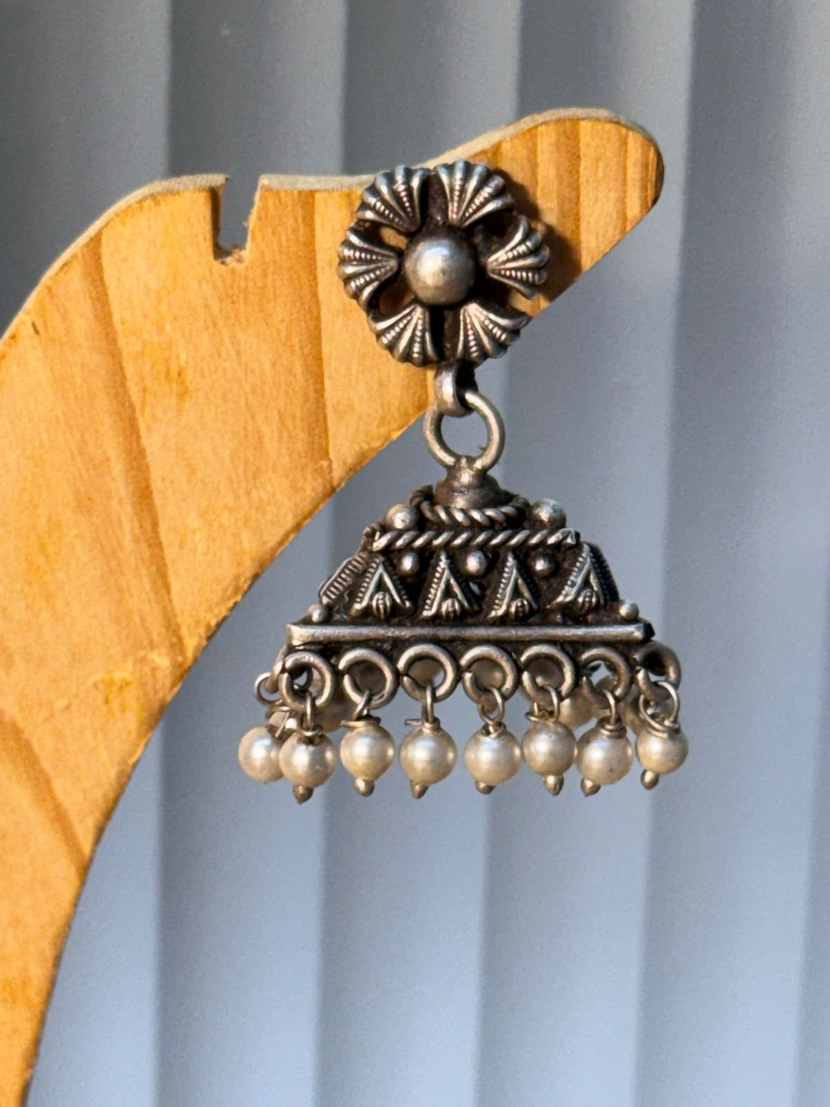 Close view of the triangular dome jhumka, showing the floral stud and the pearl fringe.