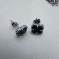 Pair of sterling silver stud earrings with green glass clovers in beaded frames, on a pale surface.