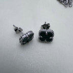 Pair of sterling silver stud earrings with green glass clovers in beaded frames, on a pale surface.