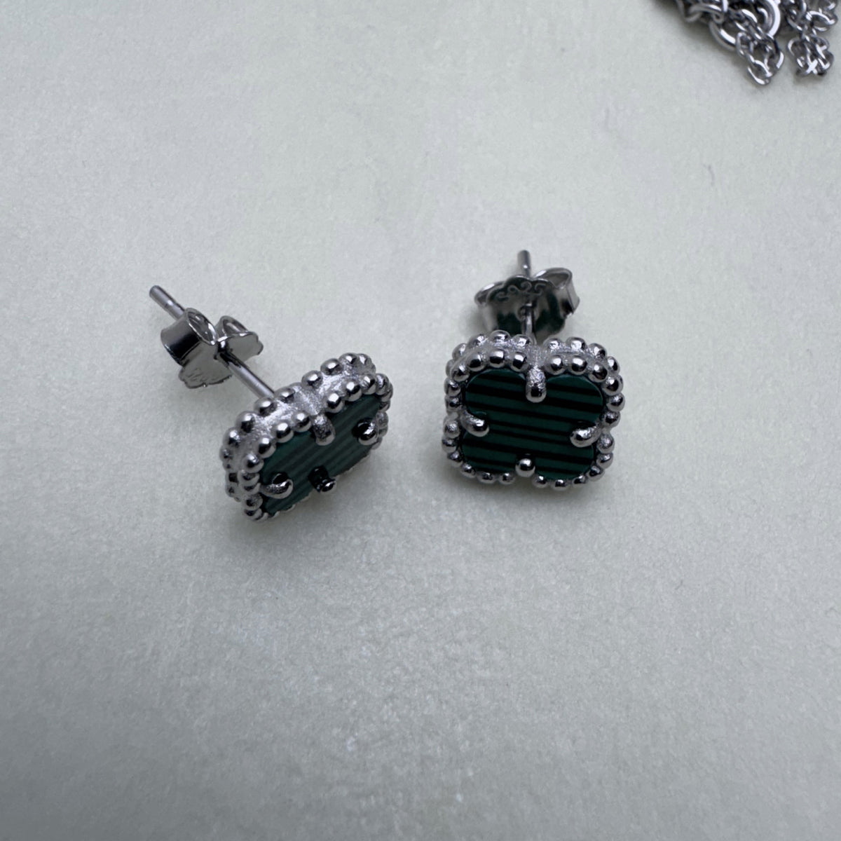 Pair of sterling silver stud earrings with green glass clovers in beaded frames, on a pale surface.