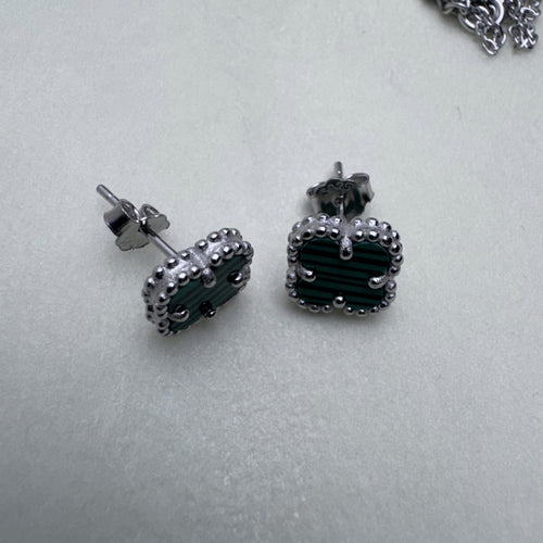 Pair of sterling silver stud earrings with green glass clovers in beaded frames, on a pale surface.