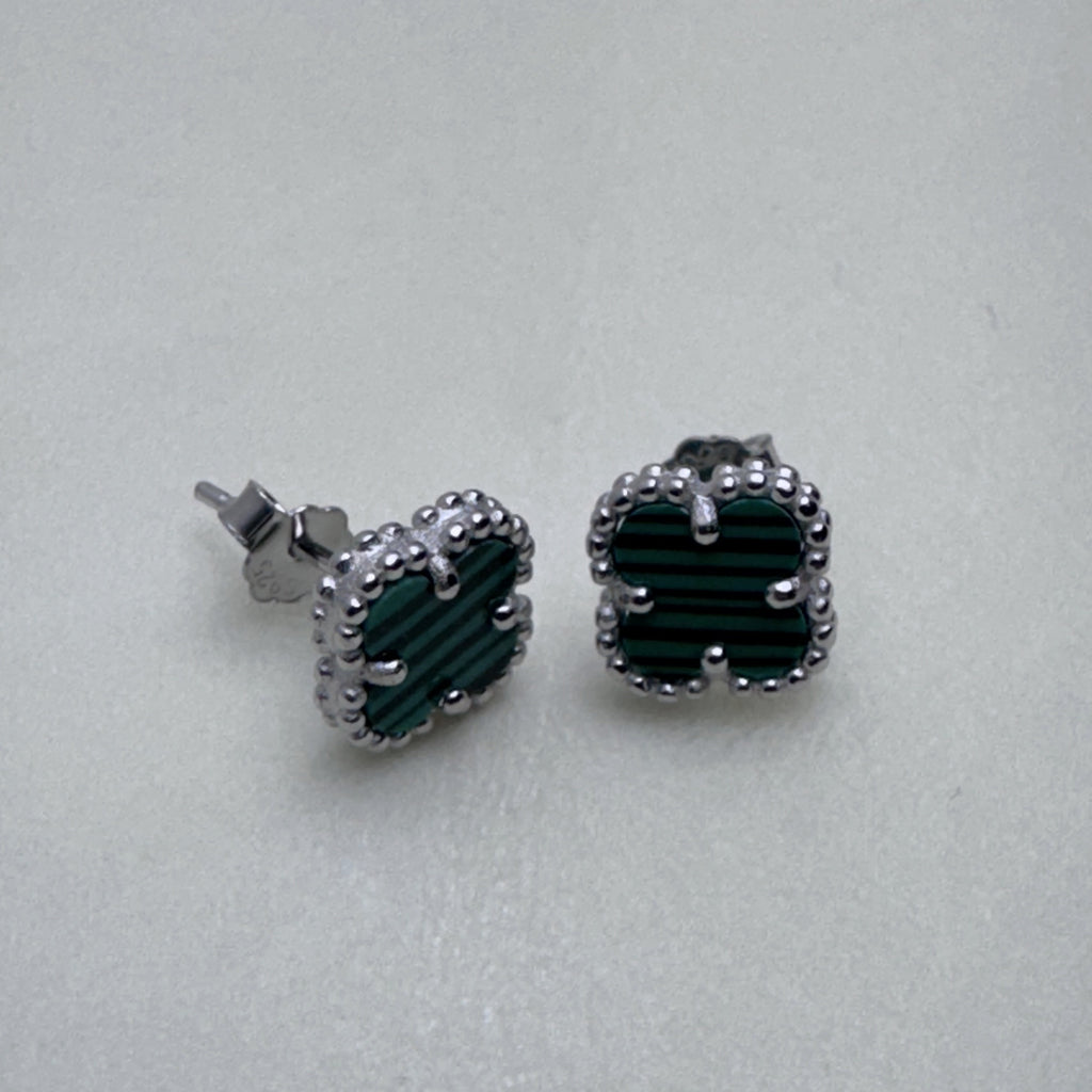 The green clover studs seen from a slight angle, showing the prongs on the clovers.