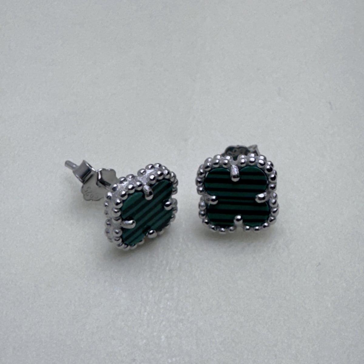 The green clover studs seen from a slight angle, showing the prongs on the clovers.