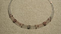 Close view of a three-strand sterling silver necklace with rose gold-tone wire sections and clusters of faceted beads, on beige woven fabric.