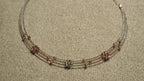 Close view of a three-strand sterling silver necklace with rose gold-tone wire sections and clusters of faceted beads, on beige woven fabric.