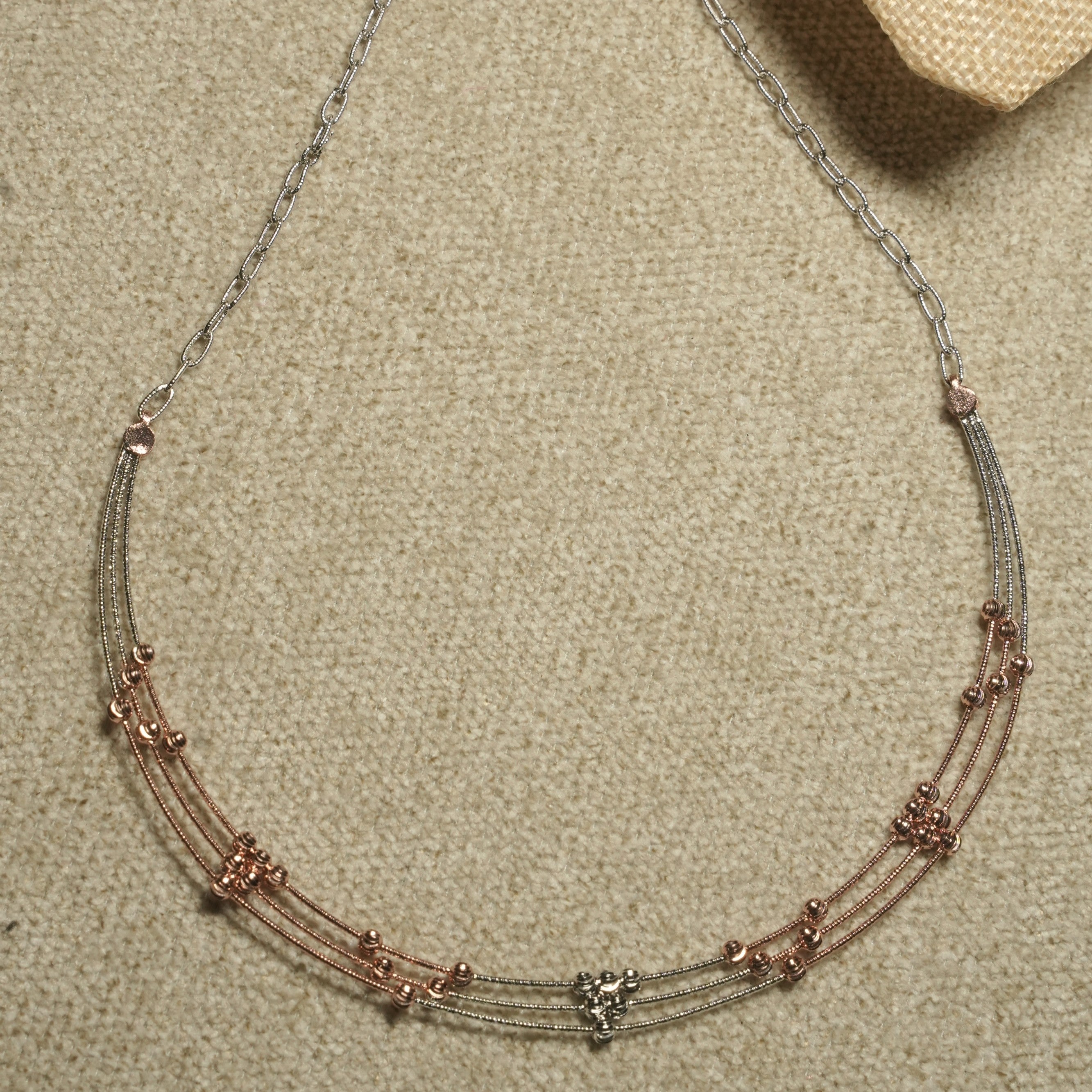Overhead view of the complete necklace with its three beaded strands meeting a fine chain that tapers to the lobster clasp.