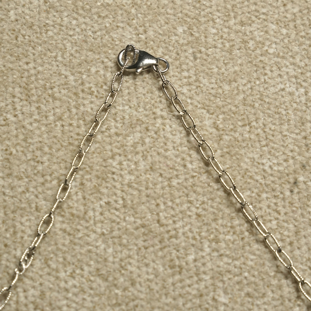 Detail of the necklace's textured sterling silver cable chain and lobster clasp against beige woven fabric.