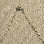 Detail of the necklace's textured sterling silver cable chain and lobster clasp against beige woven fabric.