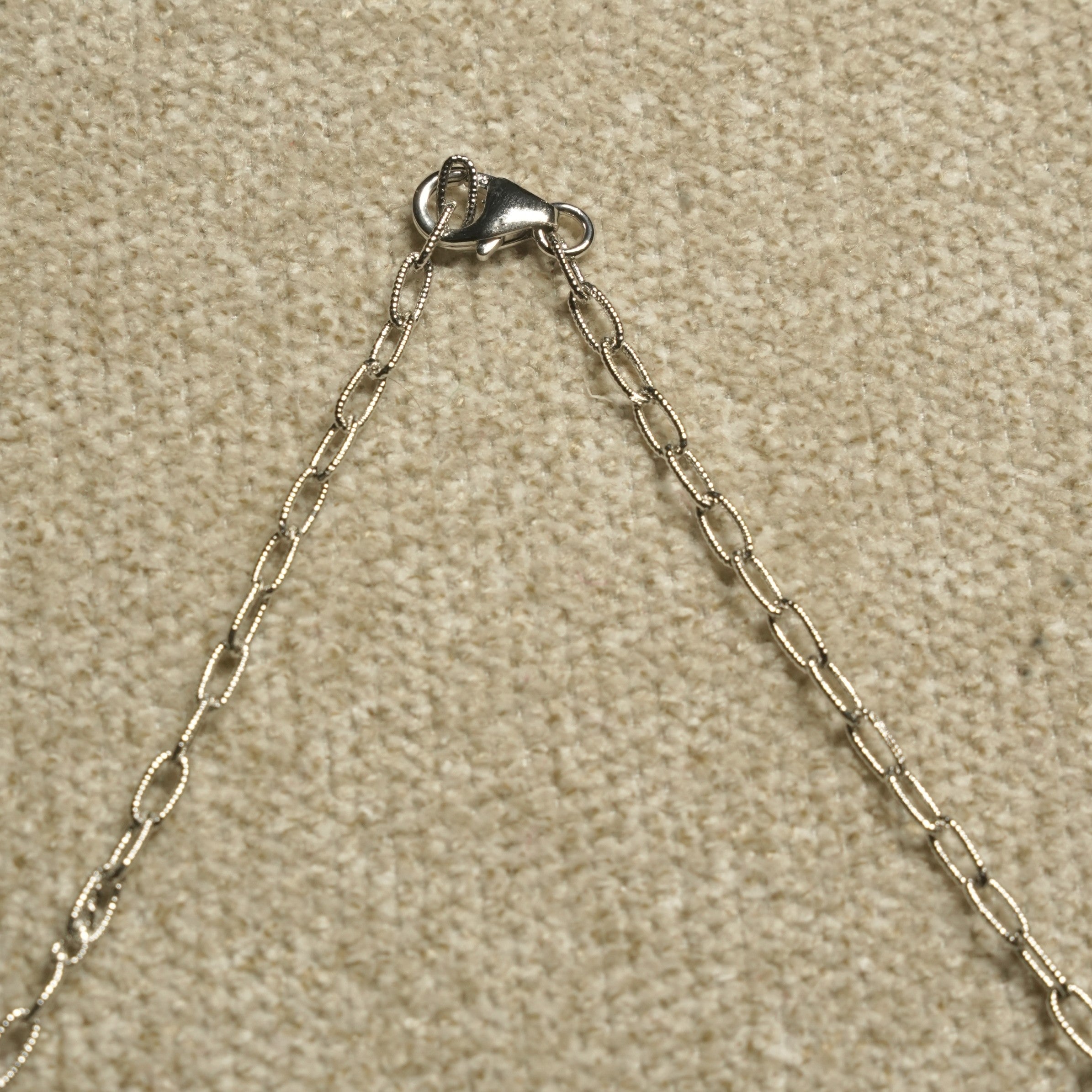 Detail of the necklace's textured sterling silver cable chain and lobster clasp against beige woven fabric.