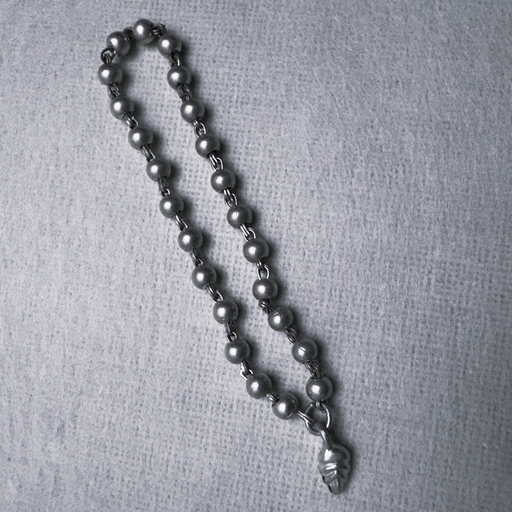 Sterling silver bead mala for a small idol with an engraved leaf drop, large size, on a grey surface.